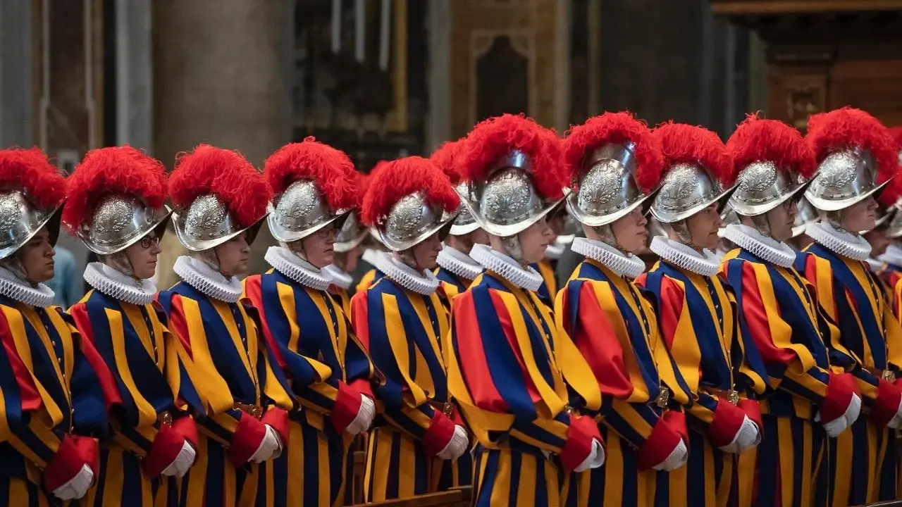 Guardia svizzera pontificia in divisa storica, con elmi piumati e abiti a righe blu, gialle e rosse, in posa solenne.