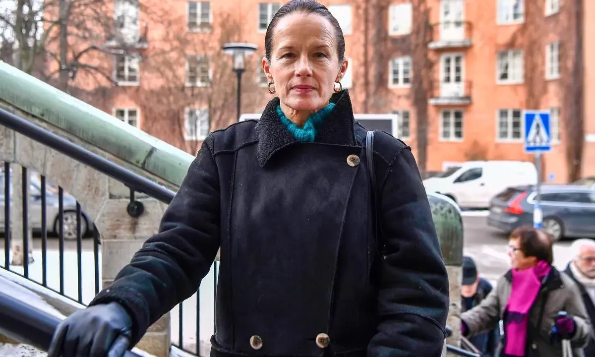 Malin Berghagen, trots att hon verkar sjuk, går uppför en trappa i en svart kappa.