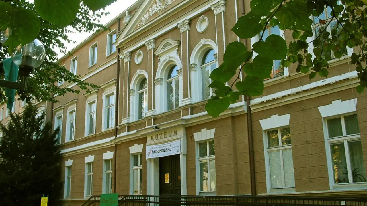 Fasada muzeum w Zielonej Górze, z napisem "MUZEUM". W pobliżu drzewa i ławka.