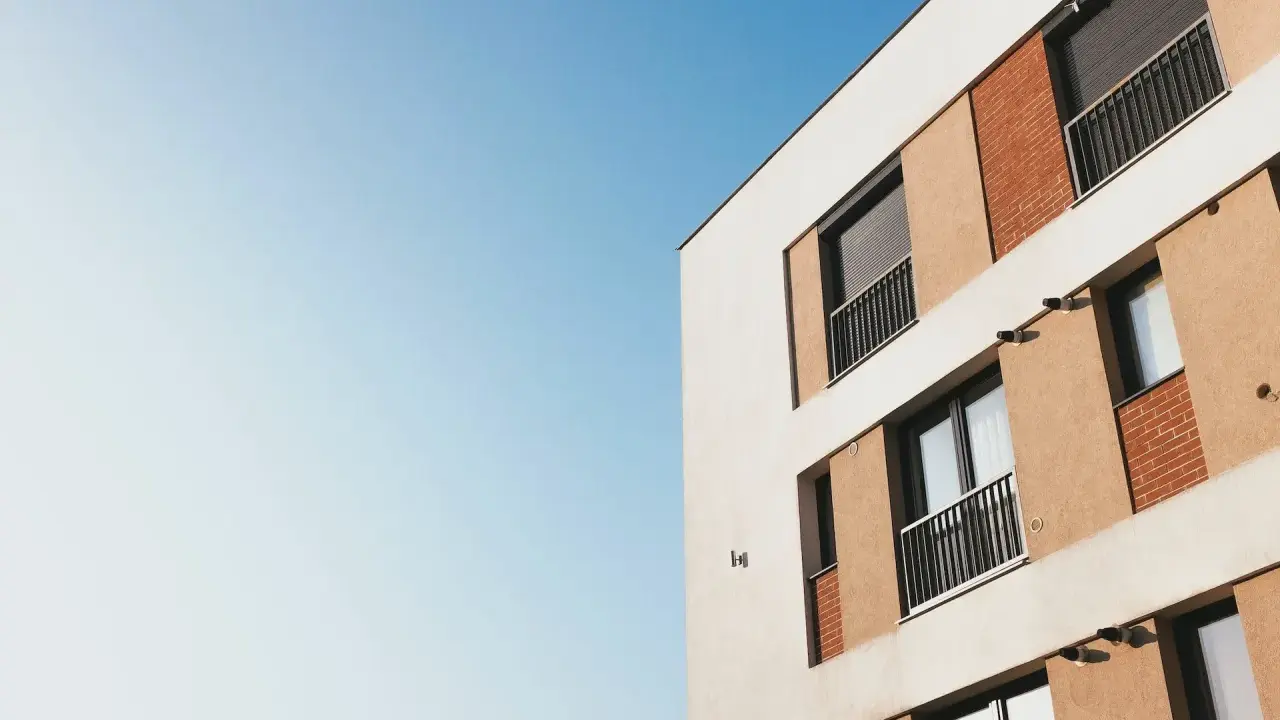 Façade d'un immeuble moderne avec balcons et volets roulants, idéal pour mettre son appartement en location. Ciel bleu clair.
