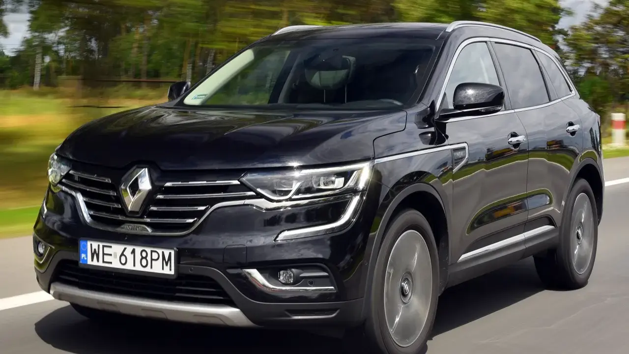 Czarny Renault Koleos 2.0 dCi pędzi po drodze, otoczony rozmytym zielonym krajobrazem.