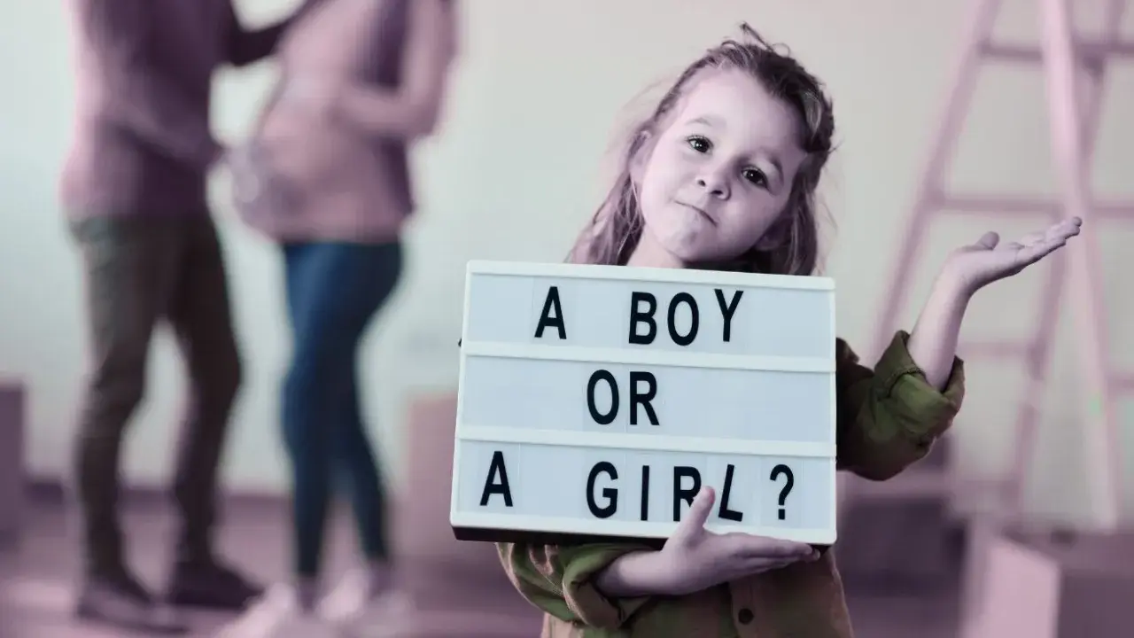Dziewczynka trzyma tabliczkę "A BOY OR A GIRL?". Rodzice czekają na dziecko, a płeć można poznać do 20. tygodnia ciąży.