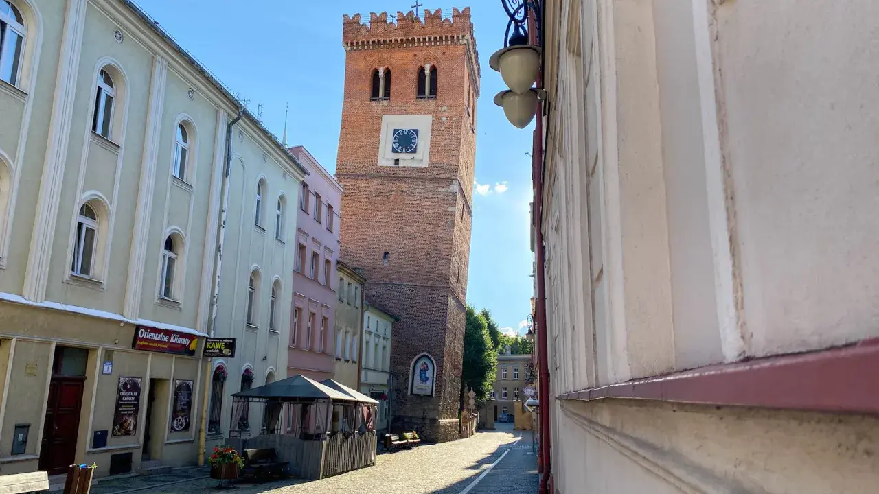 Krzywa wieża w Ząbkowicach Śląskich, ceglana, z zegarem, góruje nad brukowanym rynkiem.