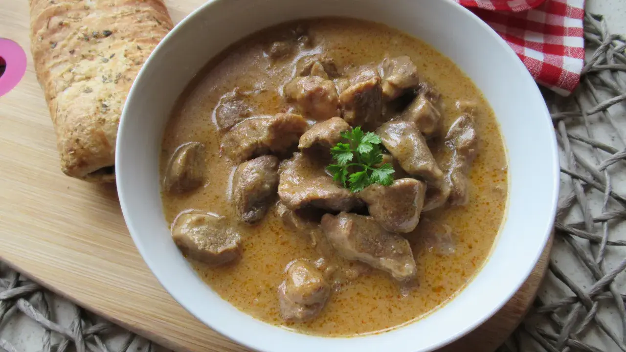 Aromaticzny gulasz wieprzowy w kremowym sosie, udekorowany natką pietruszki, podany z chrupiącym pieczywem.