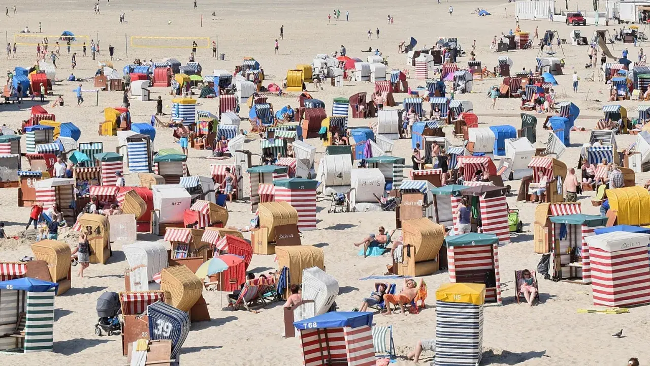 Bunte Strandkörbe säumen den Sandstrand, einige Menschen entspannen sich, andere spielen Volleyball. Ein typischer fkk strand.
