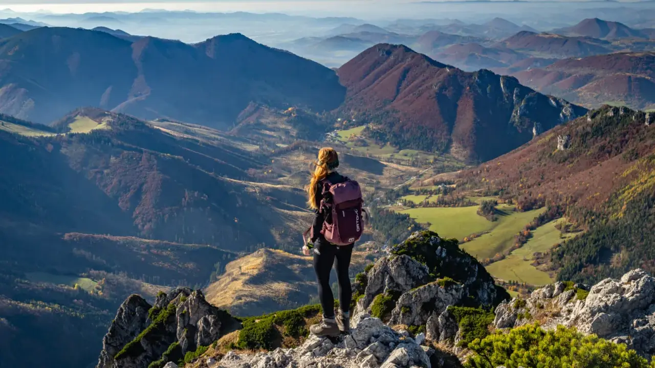 Widok na jesienne pasmo górskie Mała Fatra. Kobieta z plecakiem podziwia panoramę z kamienistego szczytu.