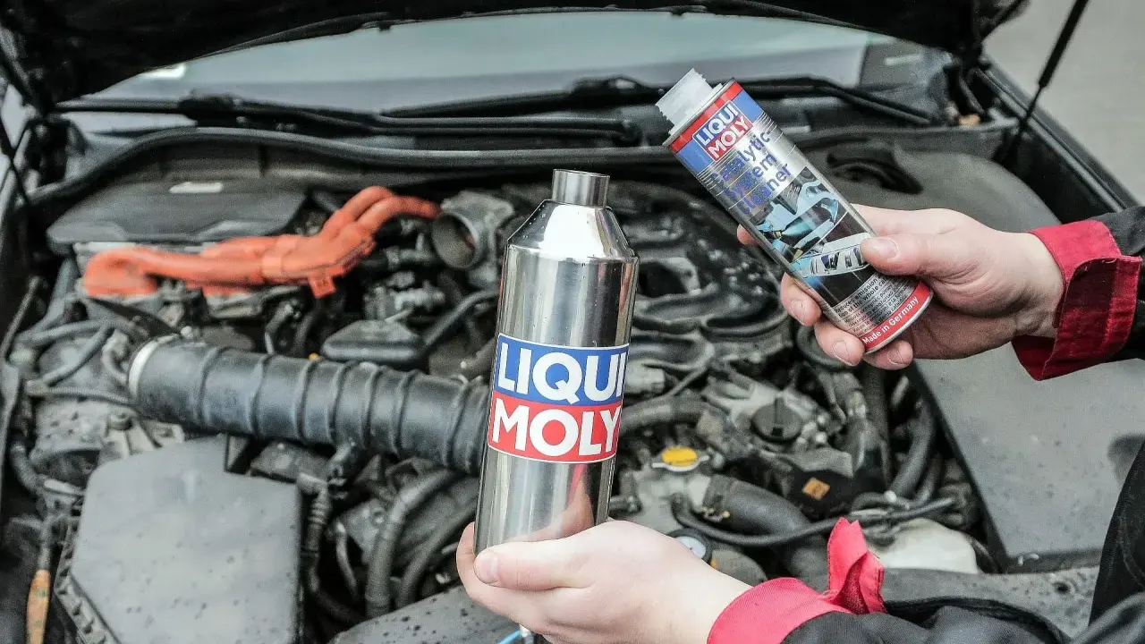 Ręce trzymające preparaty Liqui Moly do czyszczenia katalizatora. W tle widać silnik samochodu.