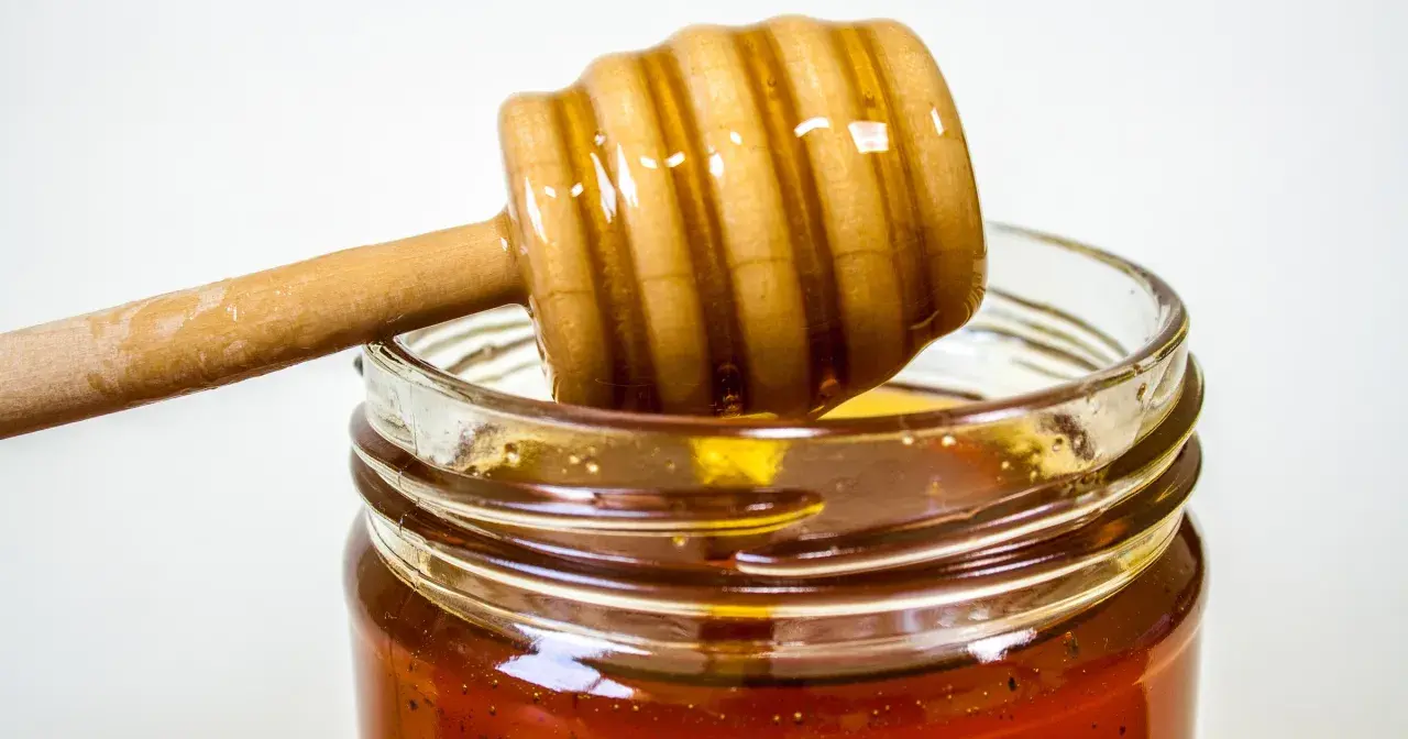 Słoik z miodem i drewniana łyżka do miodu. Naturalny antybiotyk na gardło, który pomoże złagodzić ból.
