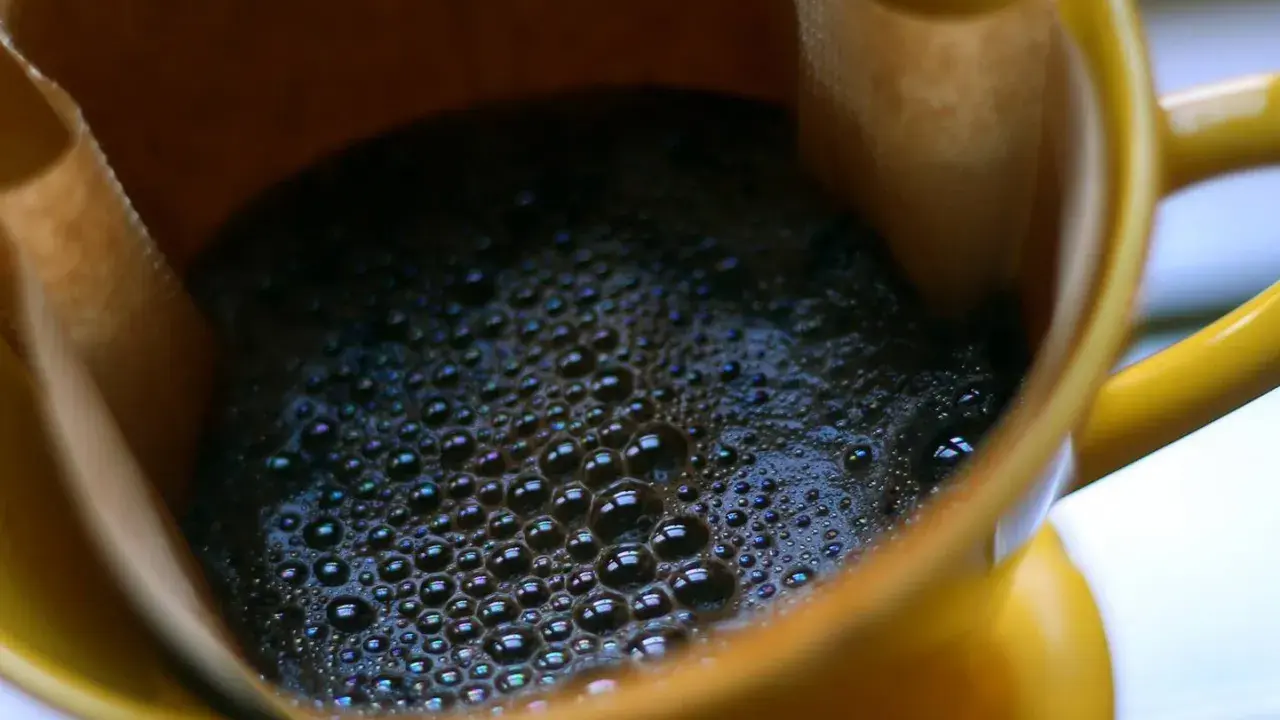 Heißer Kaffee mit Schaum in einer gelben Tasse. Ein Muntermacher, der den Unterschied zwischen Teein und Koffein verdeutlicht.
