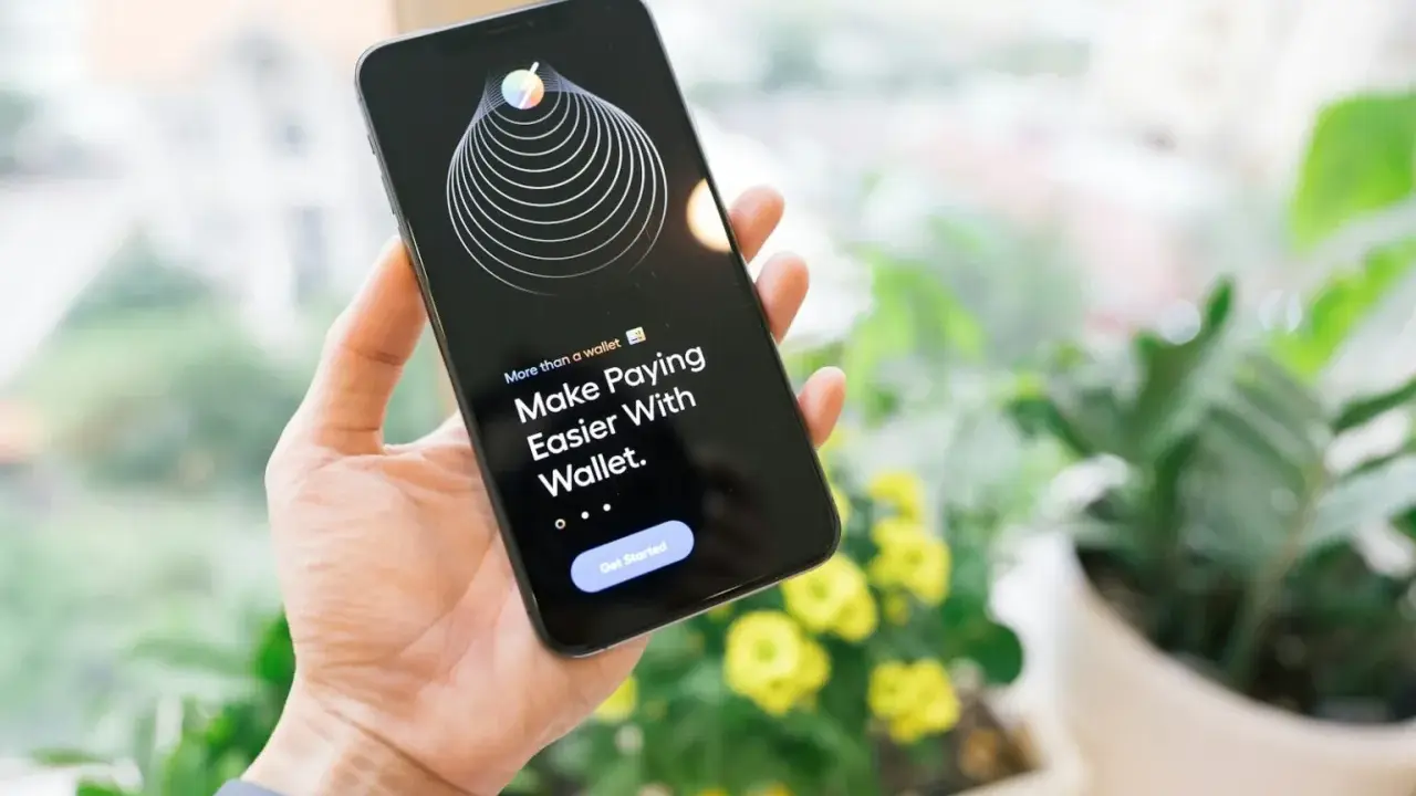 Dłoń trzyma iPhone'a z aplikacją Wallet, która ułatwia płatności dzięki technologii NFC.