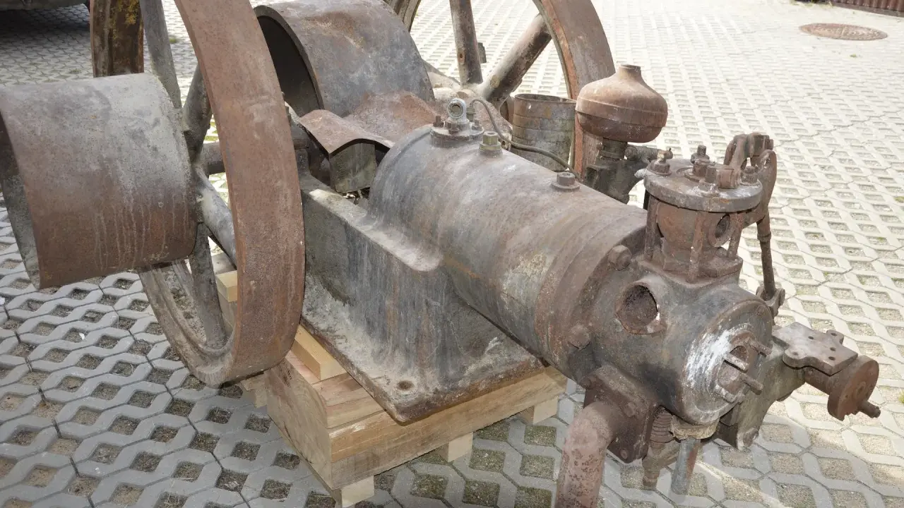 Zardzewiały silnik na gaz drzewny, z dużymi kołami, stoi na drewnianych klockach.