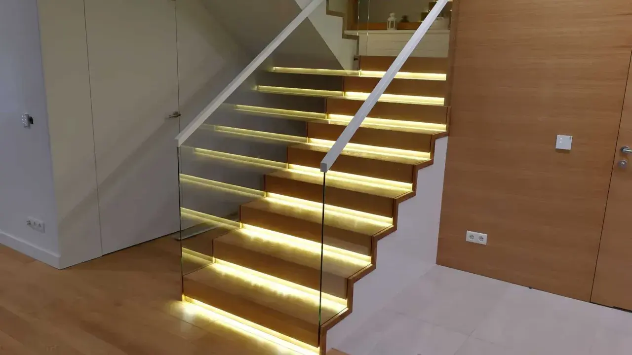 Nowoczesne schody dywanowe na beton z podświetleniem LED. Szklana balustrada i drewniane stopnie tworzą elegancką całość.