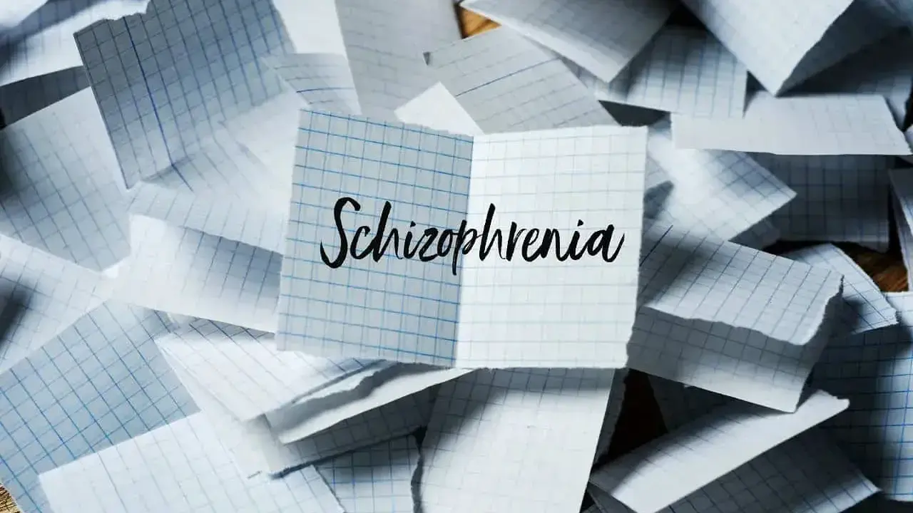 Rozrzucone kartki w kratkę, na jednej napis "Schizophrenia". Obraz symbolizuje chaos myśli, objawy schizofrenii hebefrenicznej.