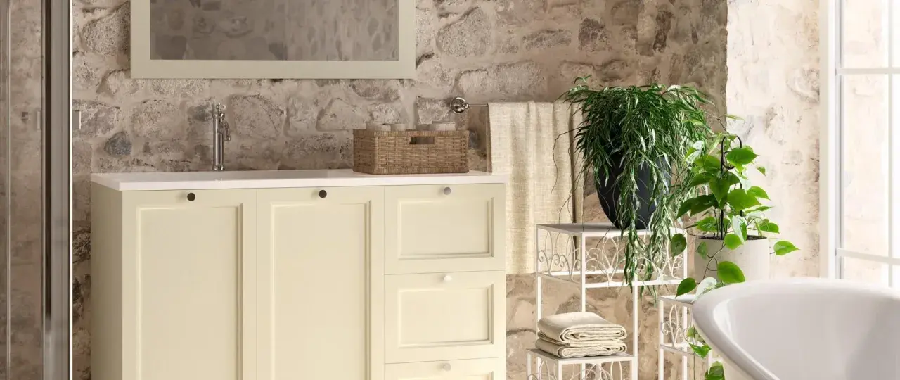 Bagni rustici di campagna con mobile lavabo color crema, cesto in vimini, piante verdi e pareti in pietra grezza.