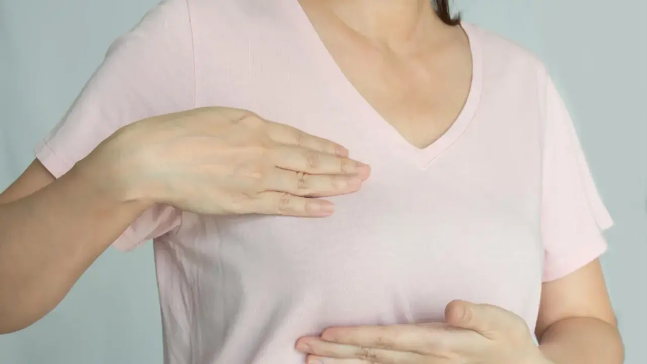 Kobieta bada swoje piersi, doświadczając bólu w piersiach, który może być związany z menopauzą.