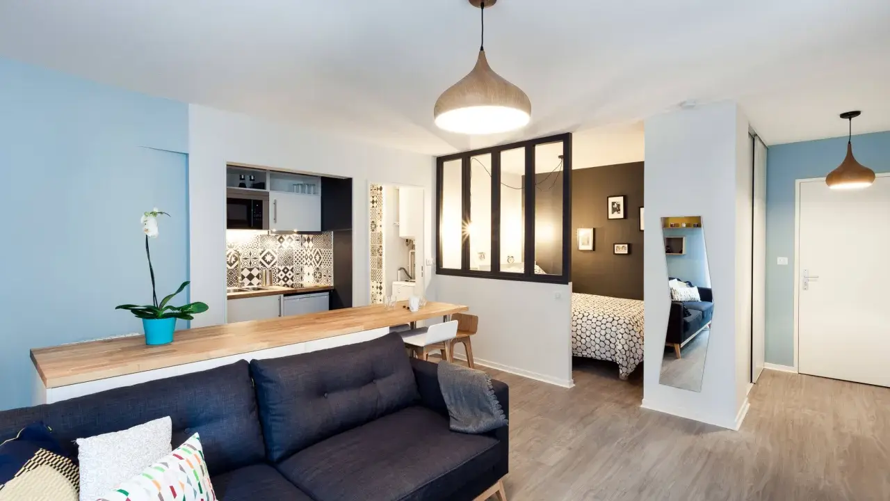 Aménagement studio 30m2 : salon cosy, cuisine moderne, chambre séparée par verrière, et coin repas.