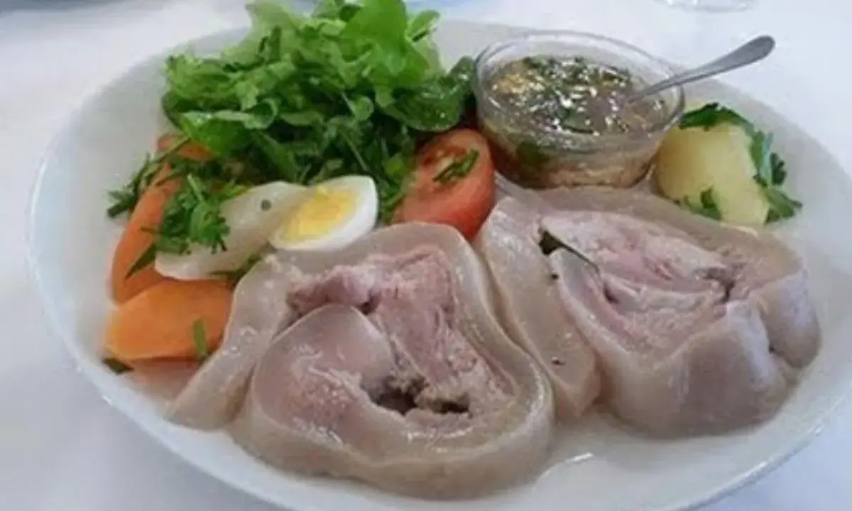 Une assiette de tête de veau gastronomique, accompagnée de légumes frais, d'un œuf dur, de carottes et d'une sauce savoureuse.