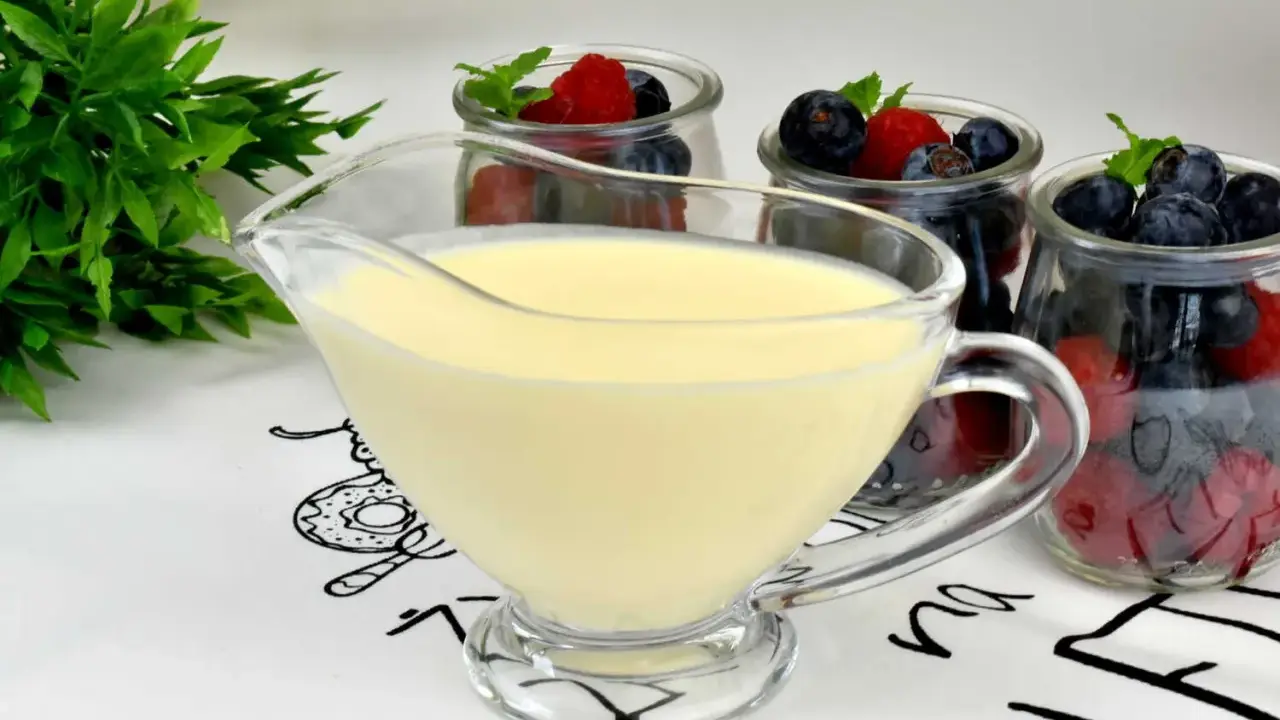 A glass boat filled with smooth, creamy krem angielski, ready to be poured over fresh berries in jars.