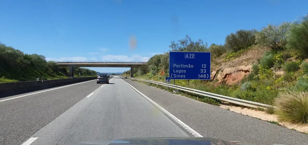 Autobahn A22 in Portugal. Ein Auto fährt auf der rechten Spur, vorbei an einem Schild mit Zielen wie Portimão und Lagos.