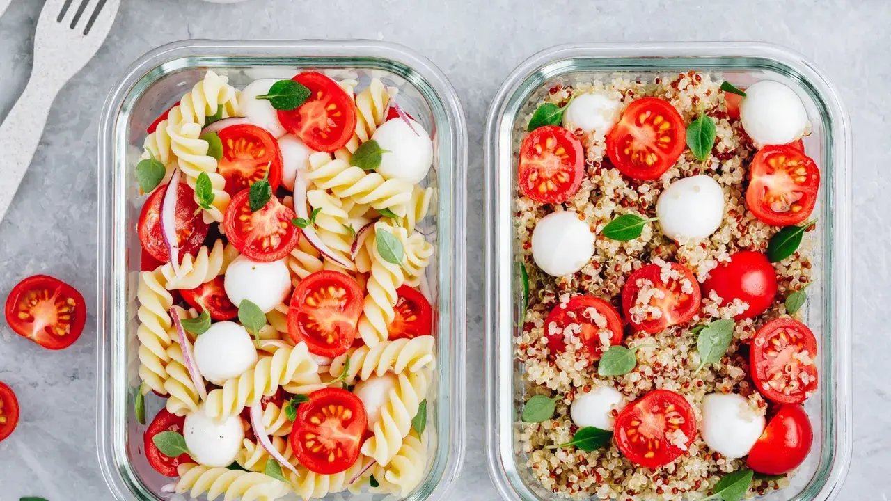 Zwei Glasbehälter mit frischen Mahlzeiten: links Nudelsalat, rechts ein bunter Quinoa-Salat mit Tomaten und Mozzarella.