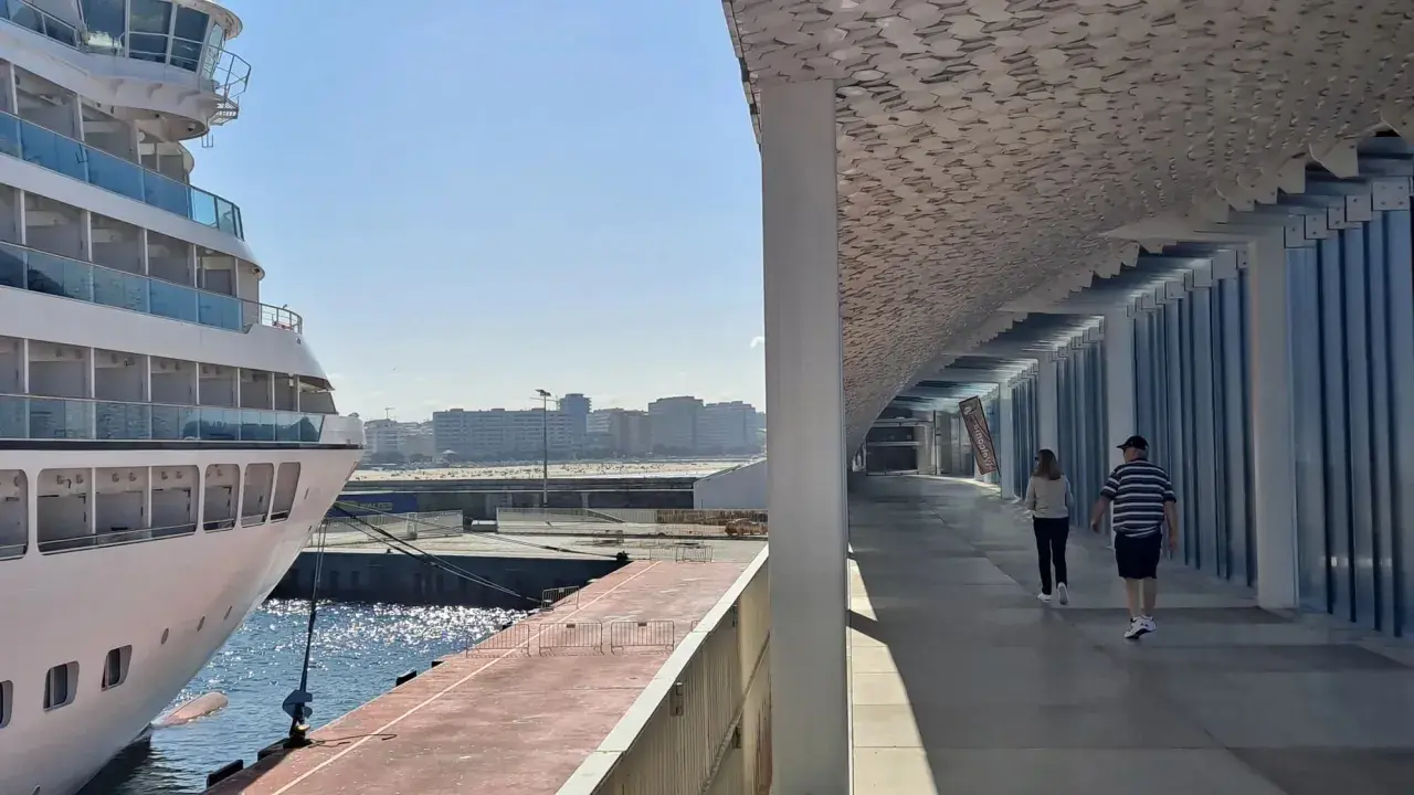 Una nave da crociera attracca nel porto di Leixões, Portogallo. Due persone passeggiano sotto una moderna tettoia con un soffitto decorato.