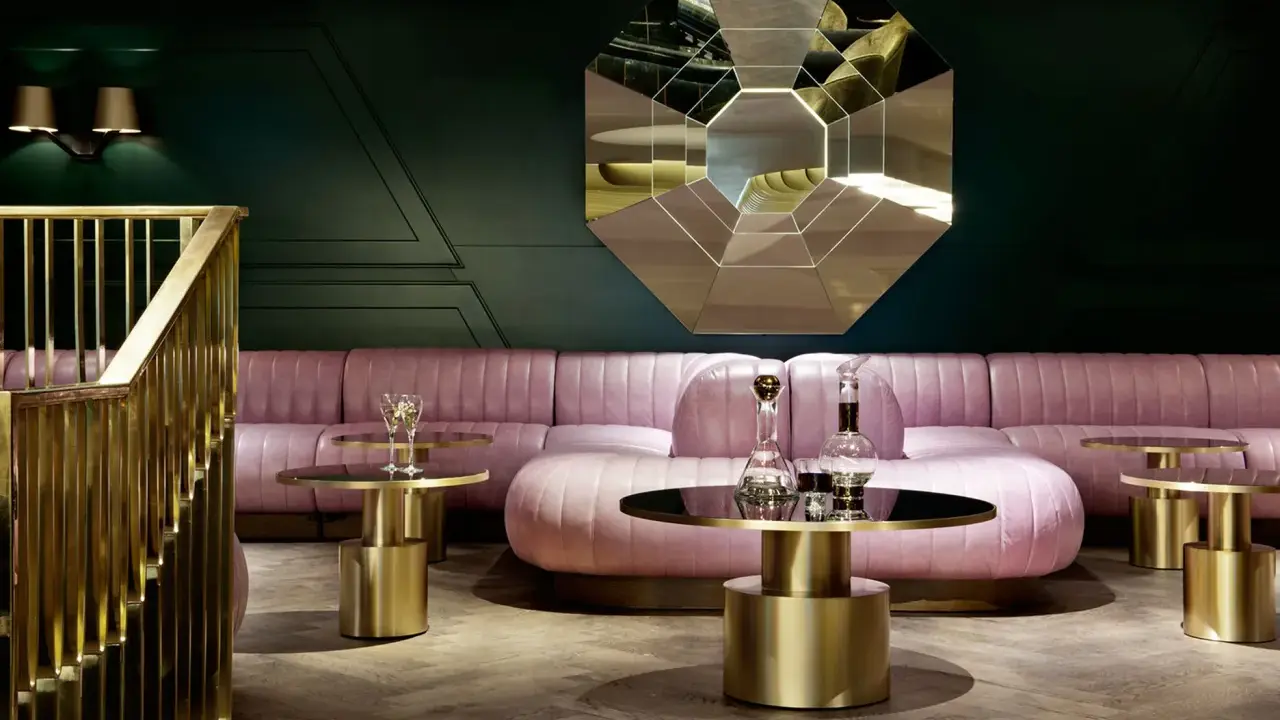Salon chic avec canapé rose poudré, tables basses dorées et miroir géométrique. Une ambiance **déco belle époque** moderne.