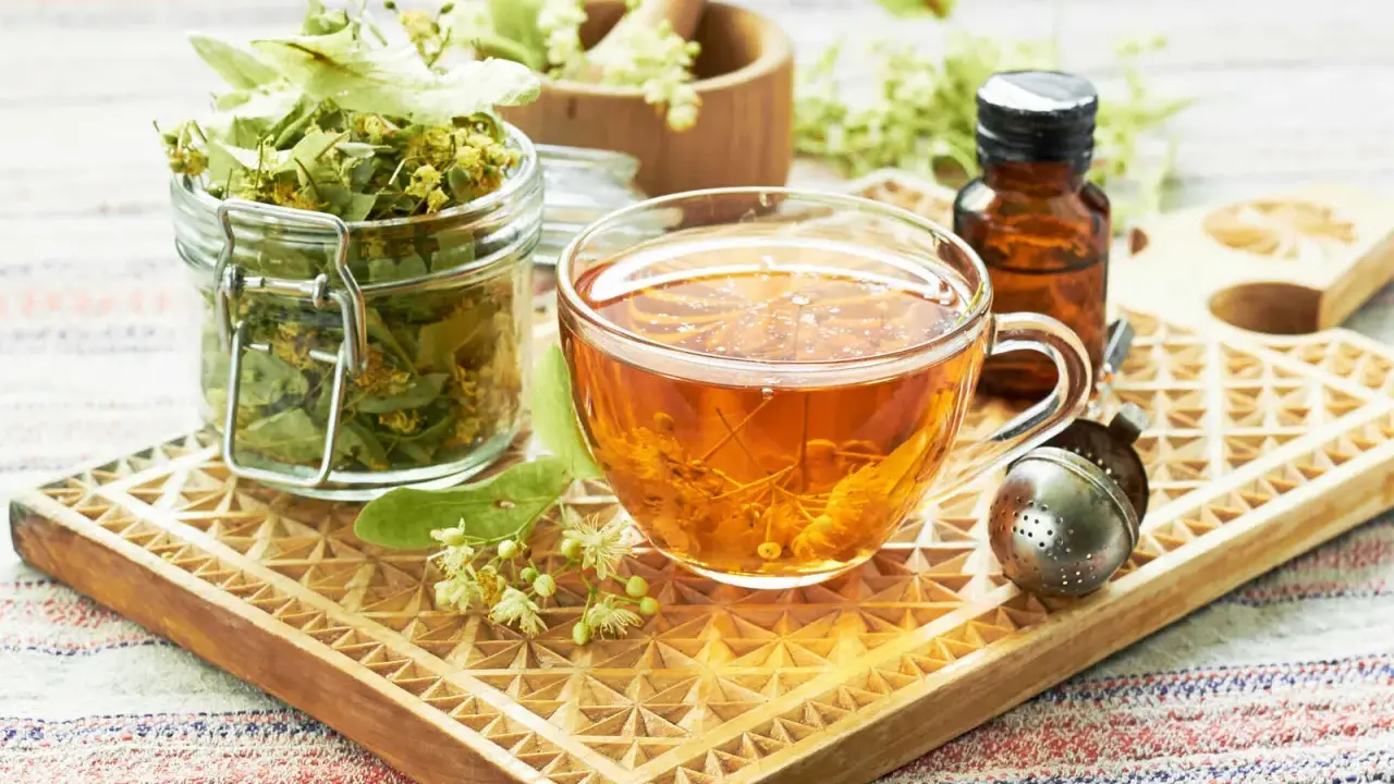 Tee aus Lindenblüten: welcher tee bei heiserkeit hilft, ist hier als dampfendes Getränk in einer Tasse, daneben getrocknete Blüten und ein Tropfenfläschchen.