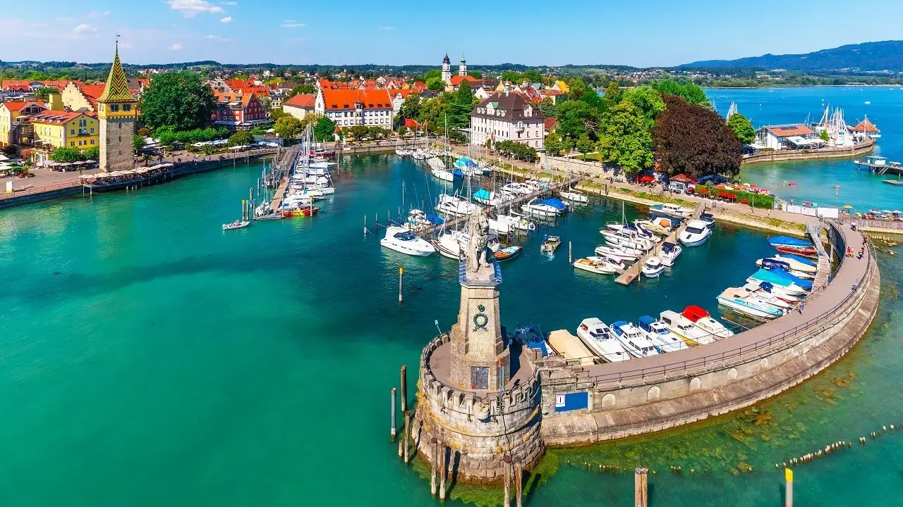Malowniczy port nad Jeziorem Bodenskim z licznymi jachtami, latarnią morską i zabytkową zabudową miasta.
