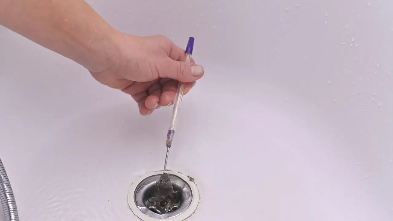 Mano retirando pelos y suciedad del desague plano de una bañera con un bolígrafo.