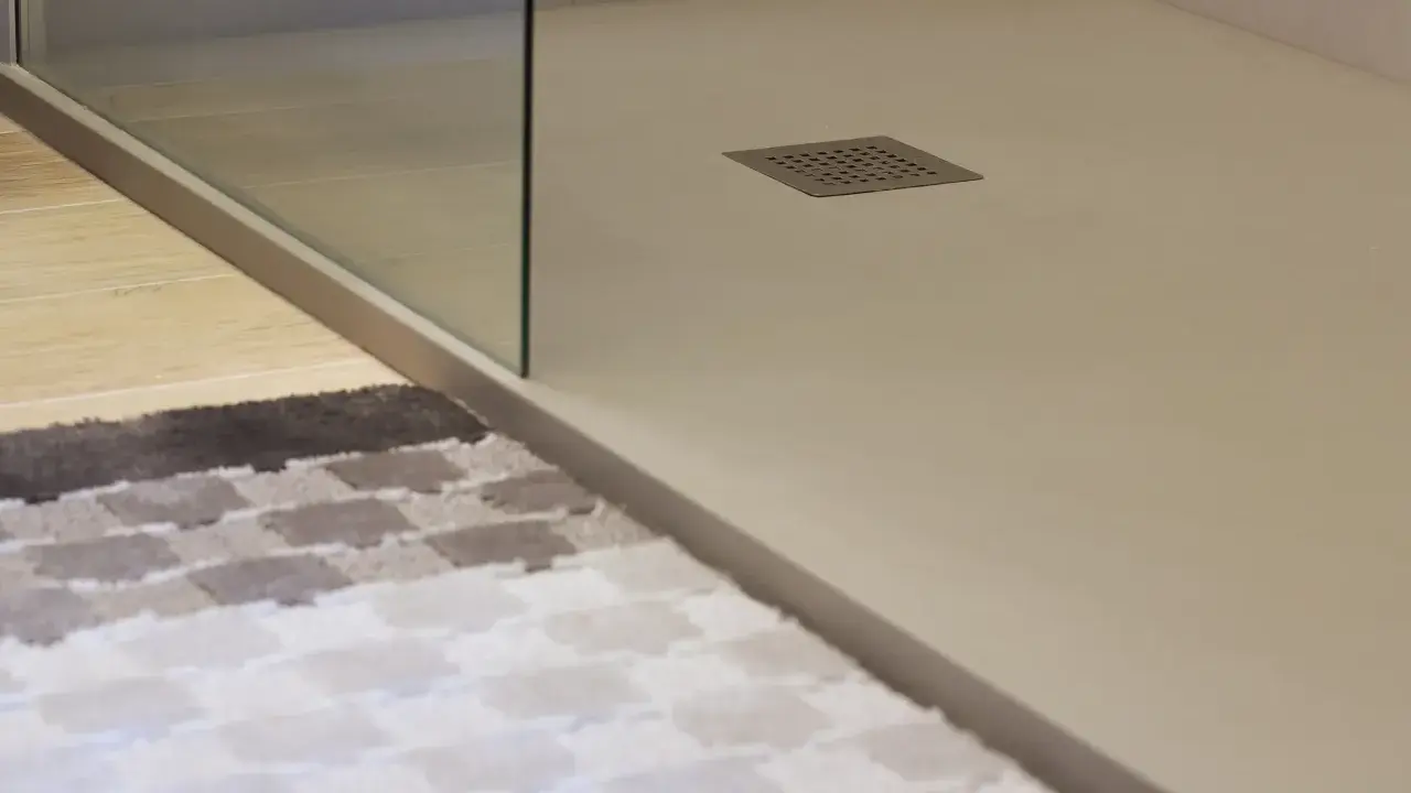 Plato de ducha de resina con desagüe cuadrado. Alfombra a cuadros en primer plano.