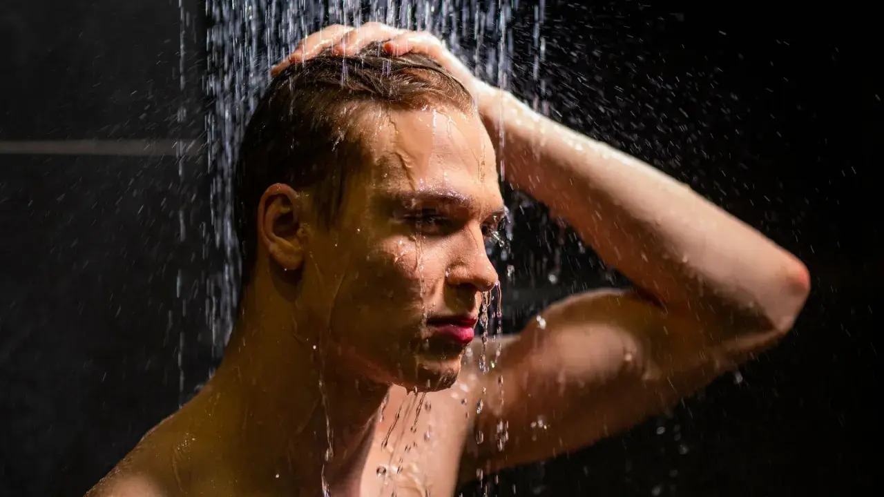 Ein Mann unter der Dusche, der sich die Haare wäscht. Die kalte Dusche ist eine Herausforderung, aber er hält durch.
