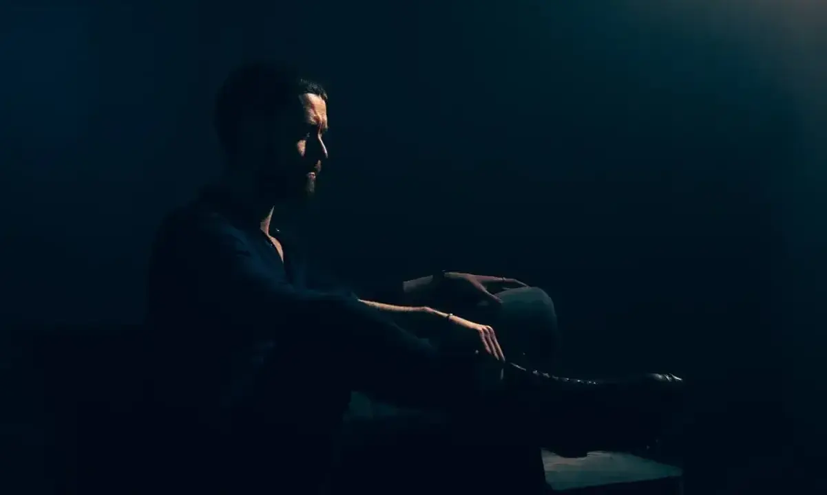 Mężczyzna w ciemnym pomieszczeniu, siedzi w fotelu. Jego sylwetka jest ledwo widoczna, podkreślona przez subtelne światło. To idealny przykład low key fotografii.