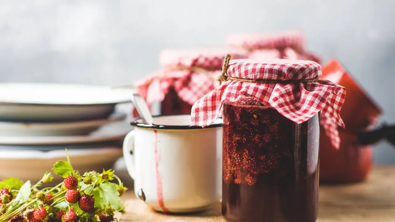 Gläser mit Erdbeermarmelade, bereit zum Marmelade einfrieren. Daneben ein Becher und frische Walderdbeeren.