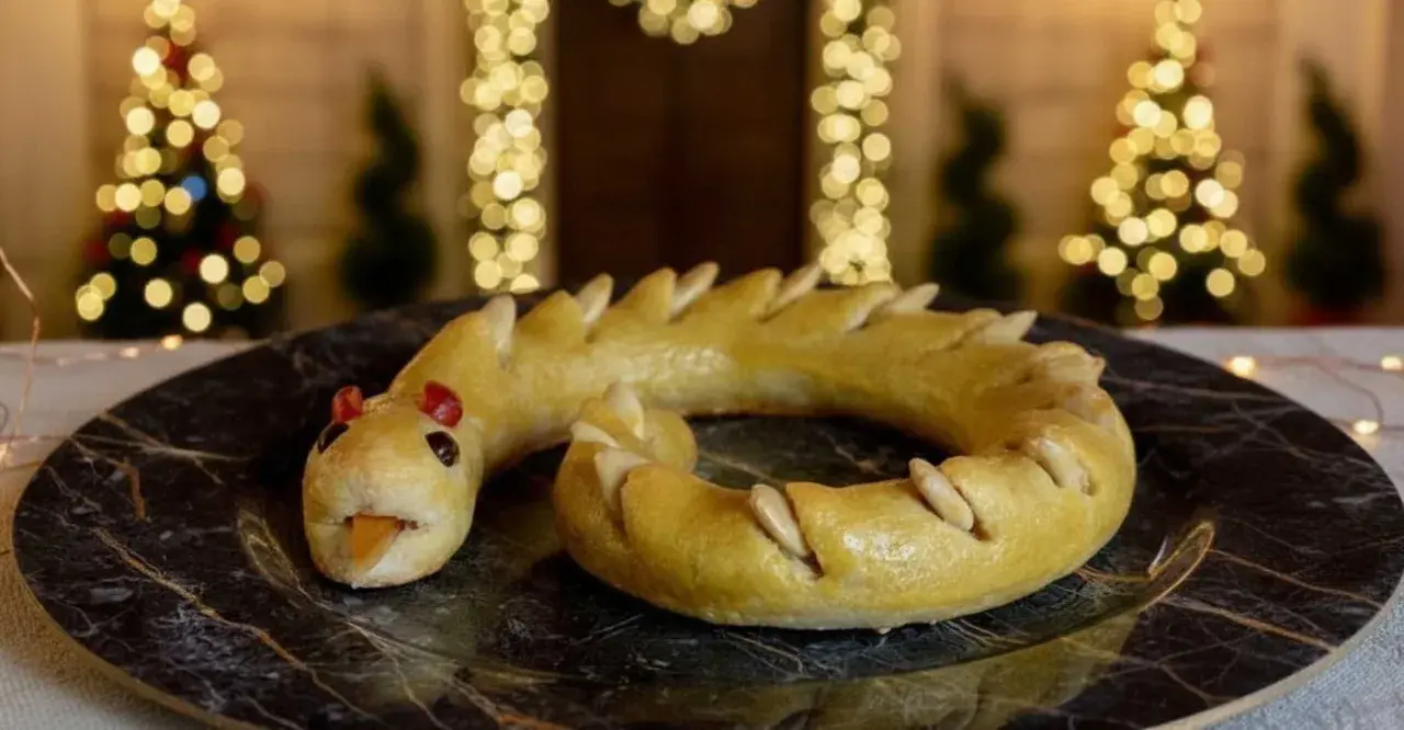 Dolci tipici Perugia: un serpente di pasta frolla dorata, con occhi rossi e lingua arancione, adagiato su un piatto scuro.