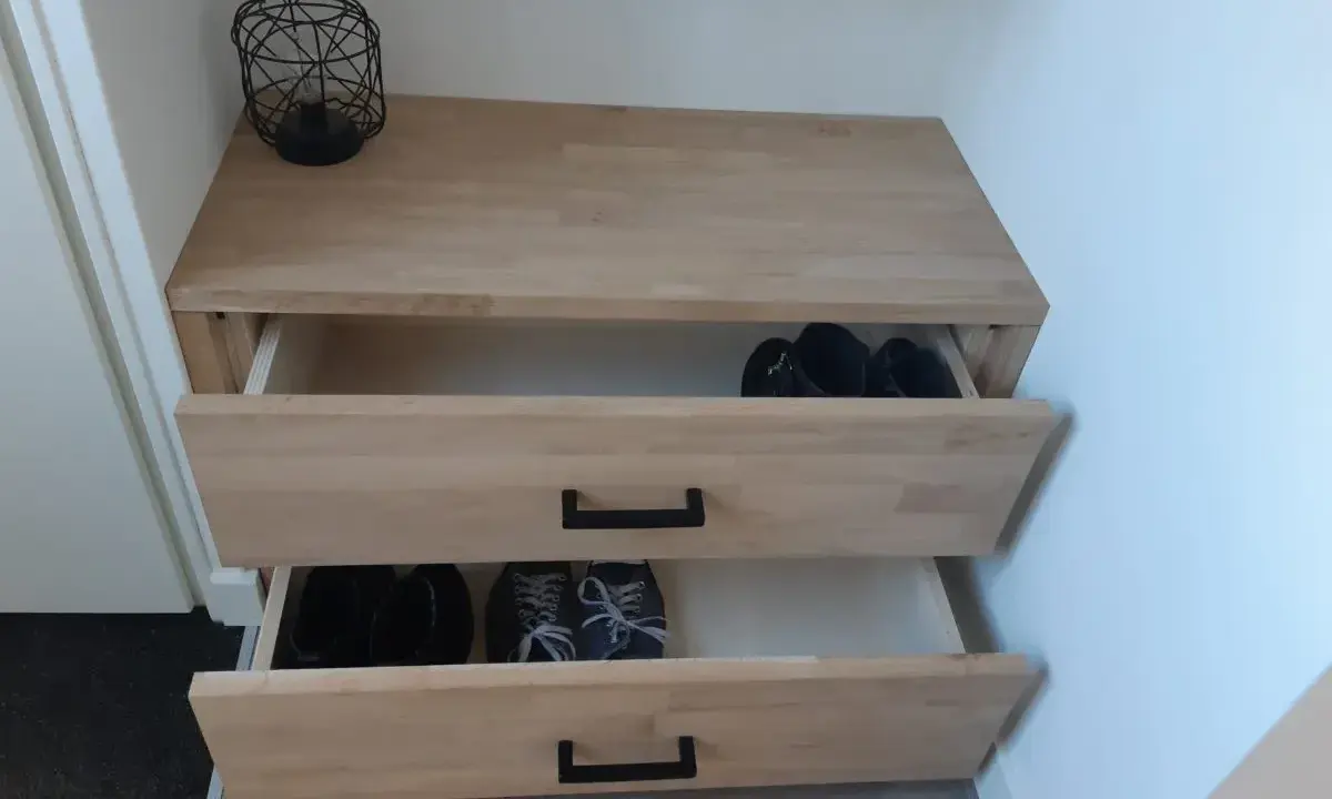 Meuble à chaussures fait maison en bois clair, avec deux tiroirs ouverts contenant des bottes et des baskets.