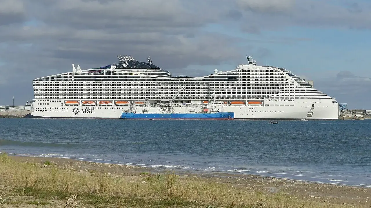 A large white MSC World Europa cruise ship docked next to a blue tanker ship in the sea.