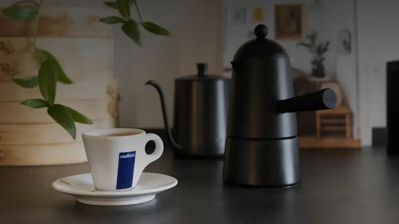 Eine Tasse Lavazza-Kaffee steht neben einer schwarzen Mokkakanne. Die Szene vermittelt die klassische italienische Kaffeezubereitung.