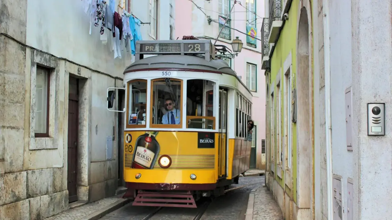 Gelbe straßenbahn lissabon fährt durch enge Gasse, Wäsche hängt über der Straße.