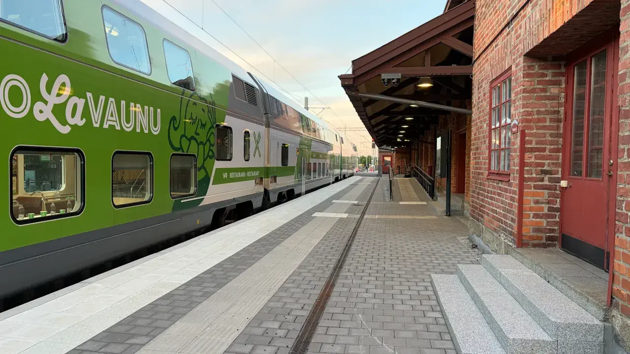 Grönt tåg med texten "LaVaunu" står vid en tegelbyggnad. Kanske är det ett tåg till Haparanda som väntar på passagerare.