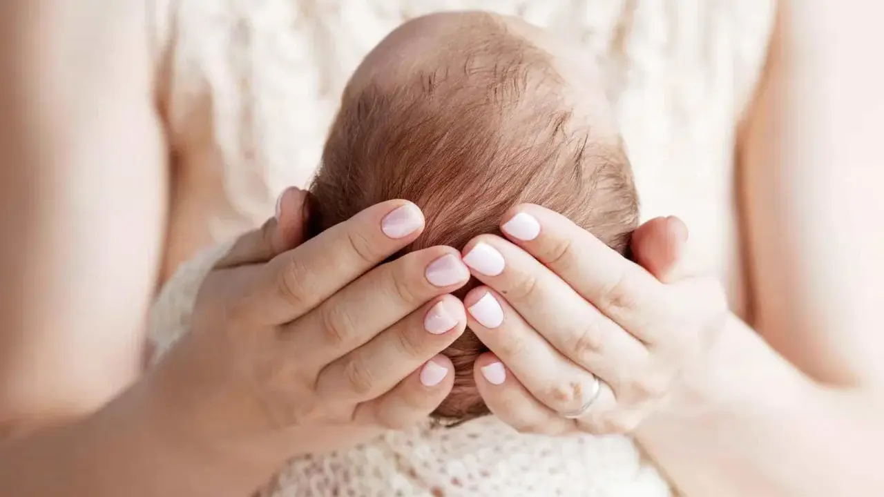 Mani delicate che accarezzano la testa di un neonato, proteggendo la sua fontanella.