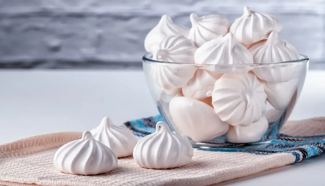 Douceur aérienne : des meringues délicates, comme préparées au bain-marie, dans un bol en verre et sur un tissu texturé.