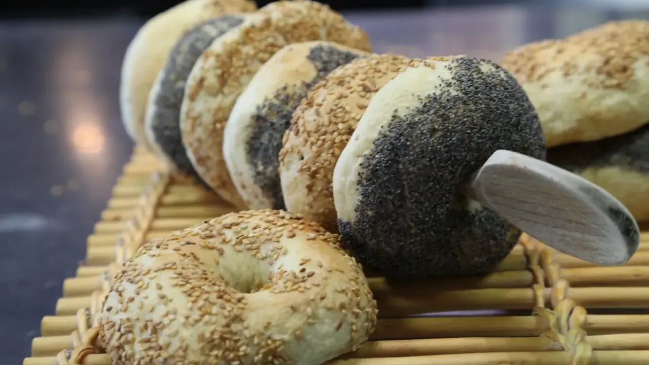 Une rangée de bagels faits maison, certains recouverts de graines de sésame, d'autres de pavot, sur une natte en bambou.