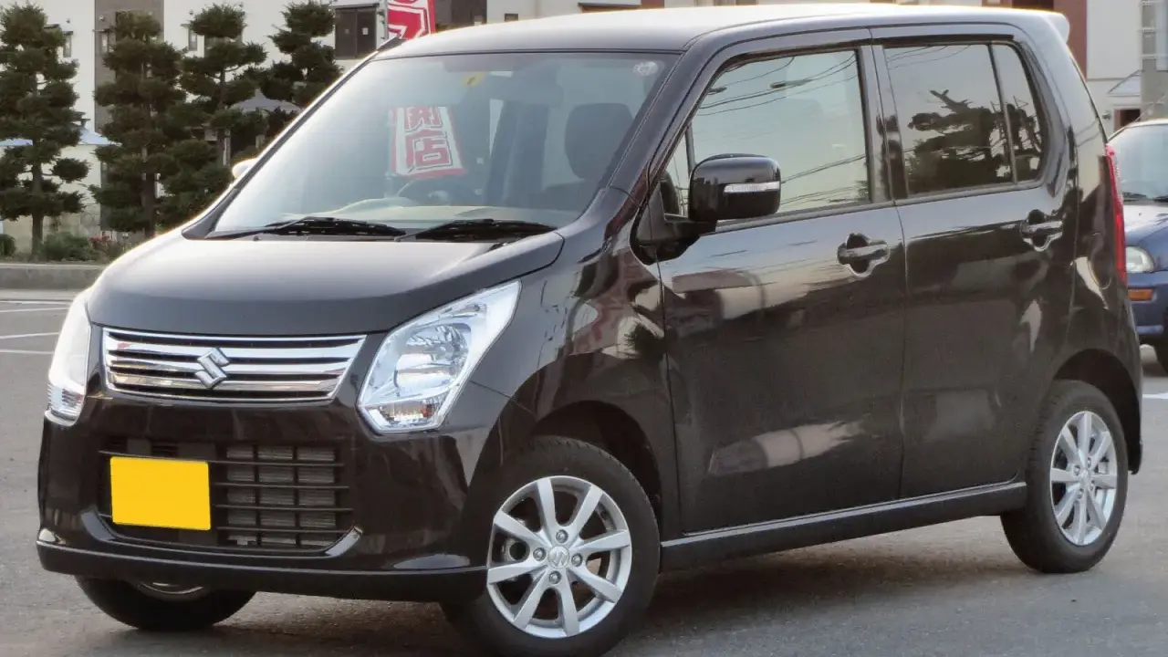 Ciemny Suzuki Wagon R+ z żółtą tablicą rejestracyjną, zaparkowany na ulicy.