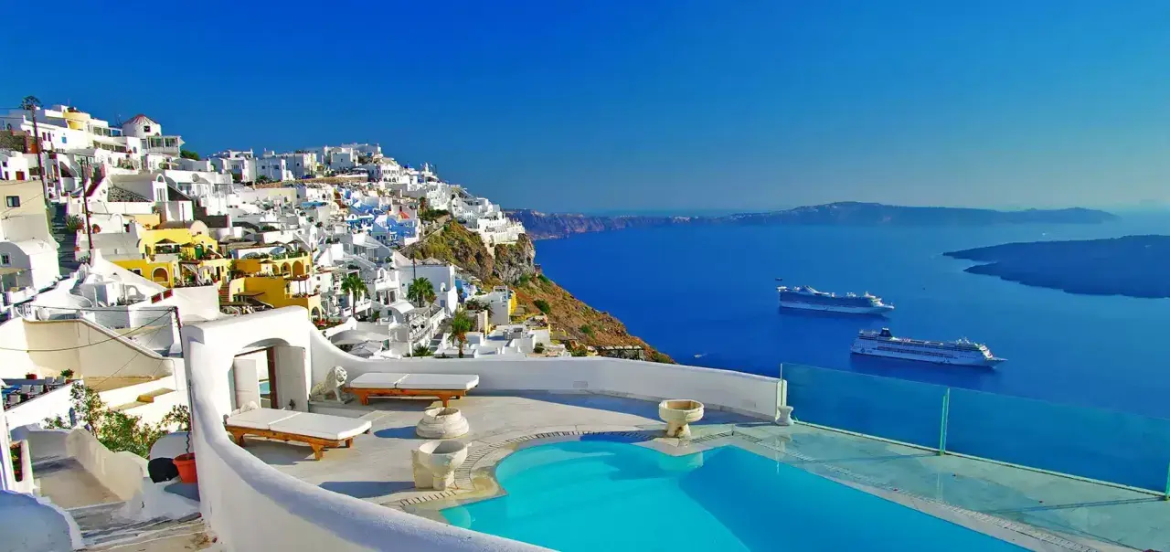 Vista mozzafiato di Santorini con case bianche a picco sul mare blu intenso. Due navi da crociera all'orizzonte, un invito a scoprire crociere a prezzi stracciati.
