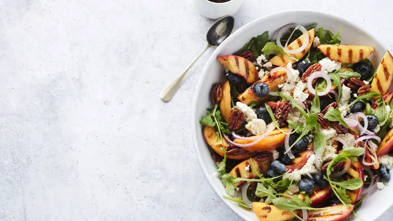 Salat mit Nektarinen, Blaubeeren, Ziegenkäse und Pekannüssen, garniert mit roten Zwiebelringen.