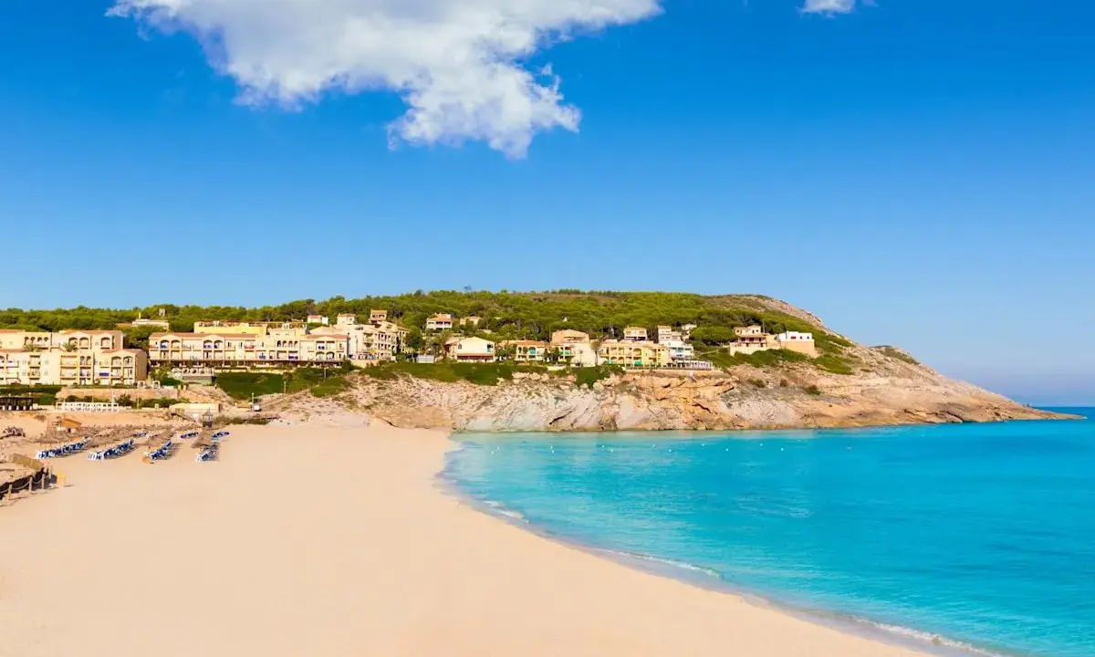 Traumhafter **Spanien Strand** mit feinem Sand, türkisfarbenem Meer und Hotels auf einem Hügel.
