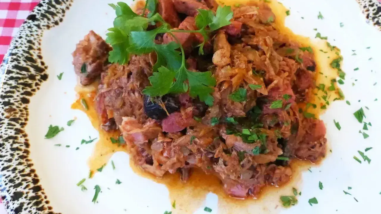 Pyszny bigos z kiszonej kapusty z kawałkami mięsa i kiełbasy, udekorowany natką pietruszki.