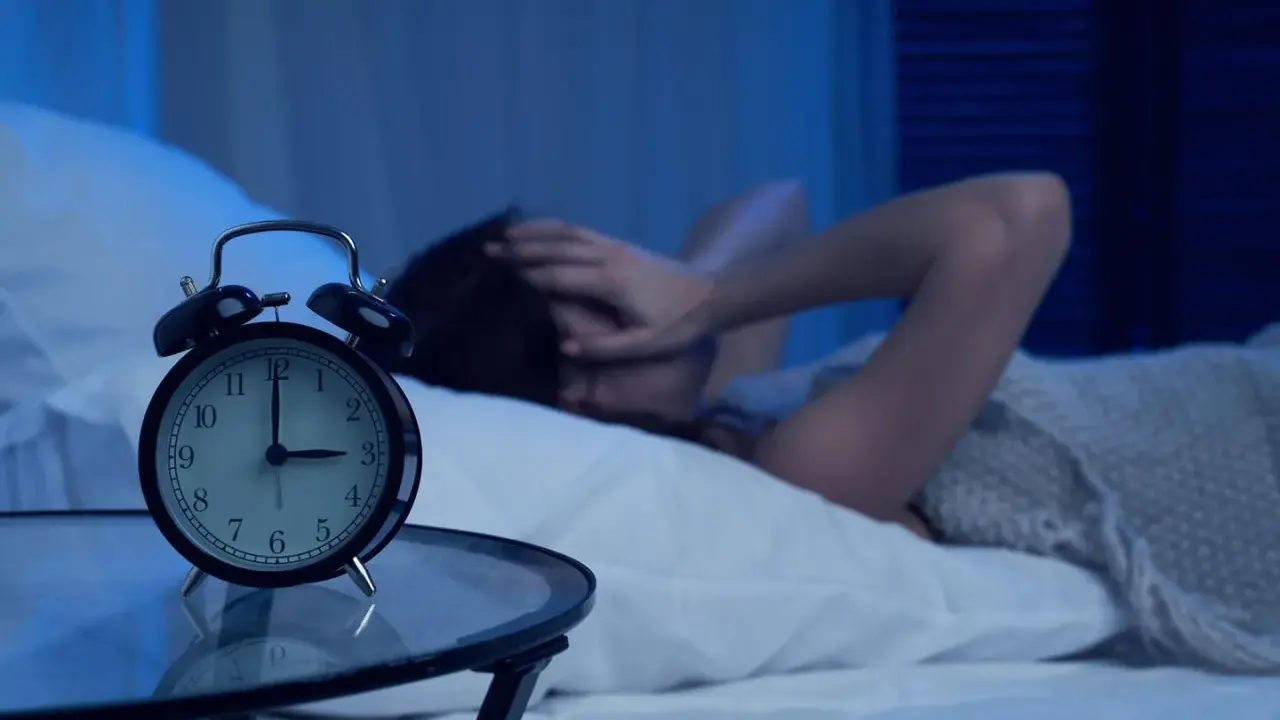 Eine Frau hält sich im Bett die Ohren zu, während ein Wecker auf 3 Uhr steht. Warum wache ich immer um 3 Uhr auf?