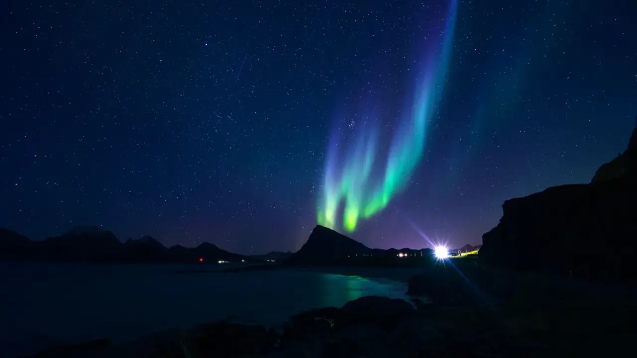Gröna och lila norrsken dansar över en stjärnklar himmel i norra Sverige. En mörk silhuett av berg och en glittrande sjö syns nedanför.