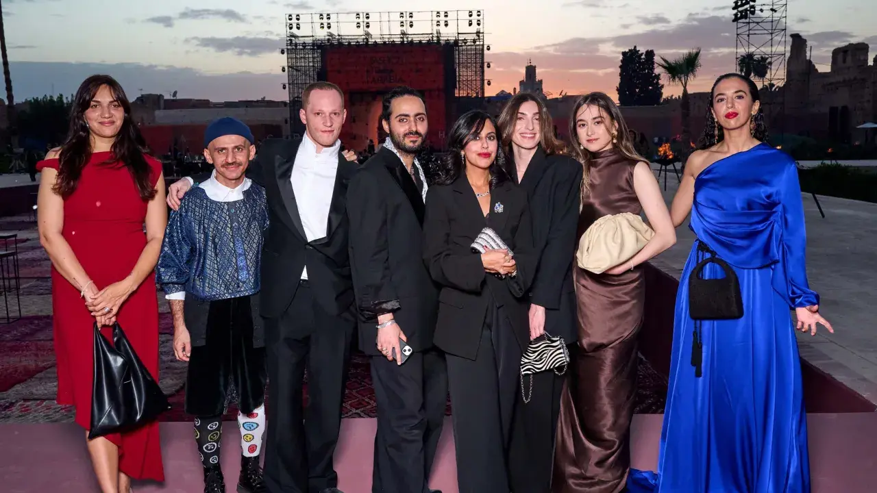 A group poses at a fashion event in Arabia. The backdrop features a large screen with "FASHION TRUST ARABIA" visible.